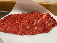 A raw beef side sirloin steak on a white paper, likely in a commercial setting such as a butcher shop or restaurant.