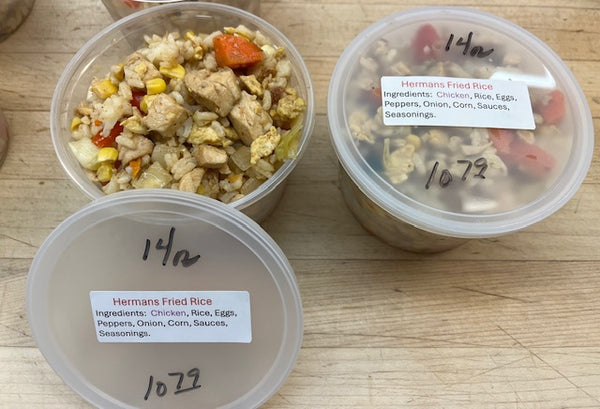 Two containers of Hermans Fried Rice on a wooden surface with labels.