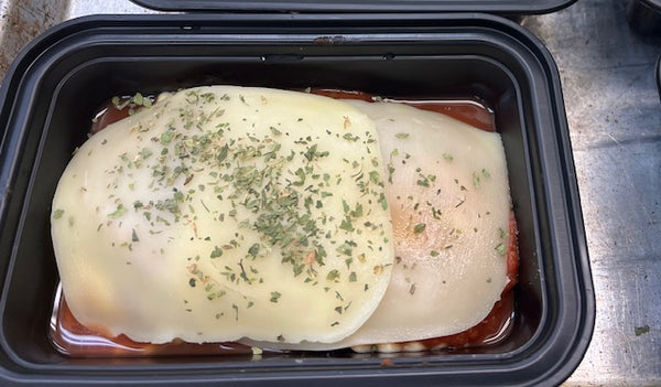 Prepared ravioli  with slice cheese on top and herbs in a black container on a metal surface
