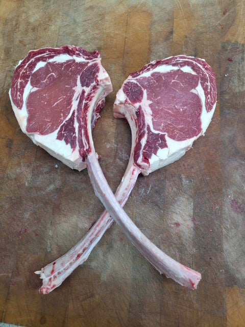 Two raw beef chops on a wooden cutting board