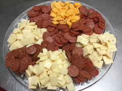 Variety of four cheeses cut up on a platter with slices of pepperoni displayed around cheeses. 