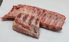 Raw baby back ribs on a white surface, cut into individual ribs.