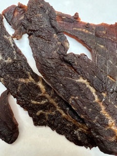 A few pieces of beef jerky with a tender, textured appearance, marinated and dehydrated on white butcher paper