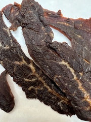 A few pieces of beef jerky with a tender, textured appearance, marinated and dehydrated on white butcher paper