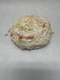A round prepared Cole Slaw on a white surface, with visible carrots and cabbage within the slaw.