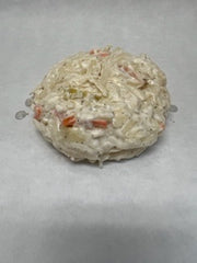A round prepared Cole Slaw on a white surface, with visible carrots and cabbage within the slaw.
