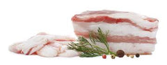 Several pieces of salt pork, also known as fatback, are laid out on a white surface with a garnish of thyme, rosemary, and other spices.