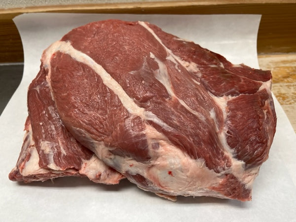 A raw lamb shoulder roast on a white plastic wrap, with visible cuts and a red hue.