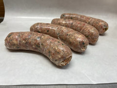 A row of sausage links laid out on a white surface, with visible seasoning.