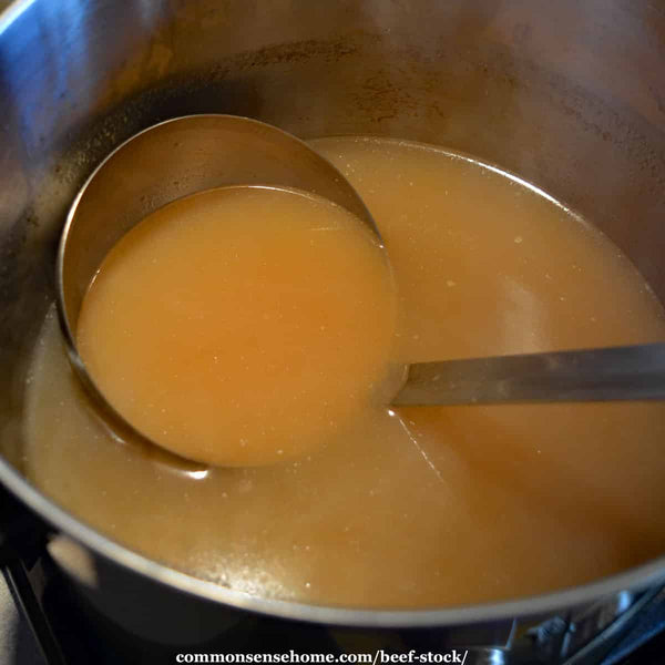 A pot on a stove with a ladle full of beef stock.