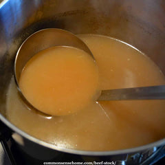 A pot on a stove with a ladle full of beef stock.