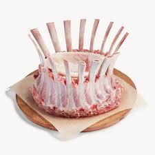 A crown roast of lamb on a wooden platter, with each ribcage pointed upwards in a circular pattern.