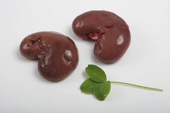 Two lamb kidneys on a white butcher paper, one of which is cut to show the inside, accompanied by a green parsley leaf