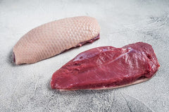 Two pieces of duck meat, one breast and one leg, on a grey surface.