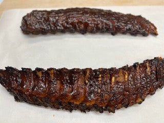 A full rack of smoked baby back ribs on white butcher paper,  ready to be heated.