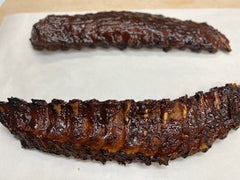 A full rack of smoked baby back ribs on white butcher paper,  ready to be heated.