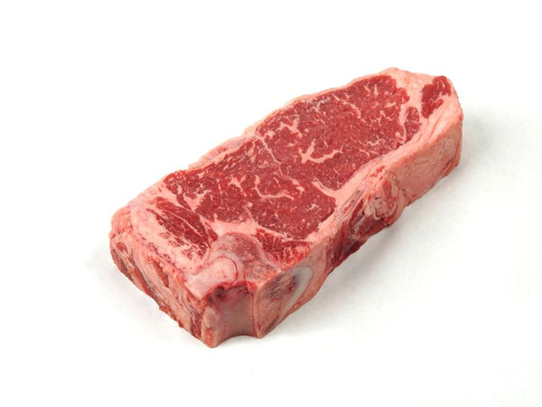 A raw shell steak,  a cut of beef with visible marbling, displayed on a white butcher paper