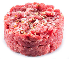 A raw beef steak tartare with visible seasonings on a white background.